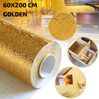 A roll of golden foil kitchen wallpaper sticker shown applied on a kitchen counter and being peeled off from a surface.